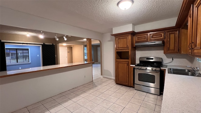 kitchen with sink, a barn door, a textured ceiling, stainless steel range with gas stovetop, and rail lighting