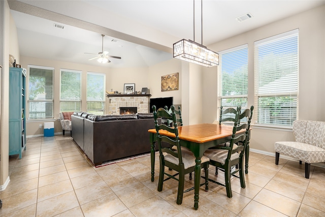 dining area with a wealth of natural light, a stone fireplace, light tile patterned floors, and ceiling fan