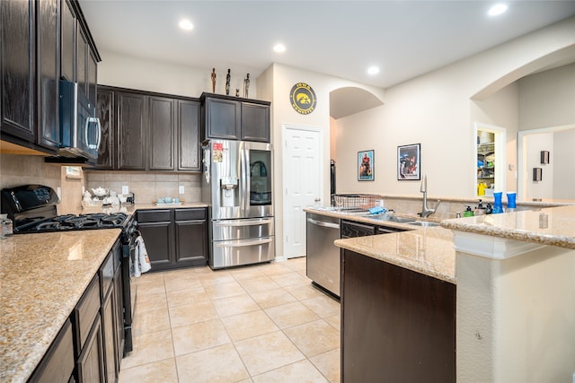 kitchen featuring decorative backsplash, light stone countertops, dark brown cabinets, and stainless steel appliances