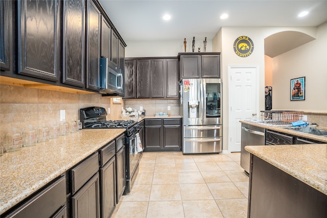 kitchen featuring dark brown cabinets, light tile patterned floors, backsplash, light stone countertops, and stainless steel appliances