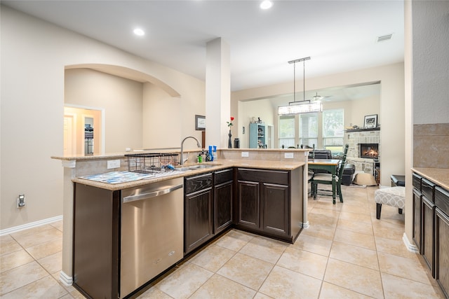 kitchen featuring sink, a stone fireplace, pendant lighting, stainless steel dishwasher, and a center island with sink