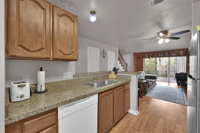 kitchen with stainless steel refrigerator, dishwasher, sink, light stone countertops, and light hardwood / wood-style flooring