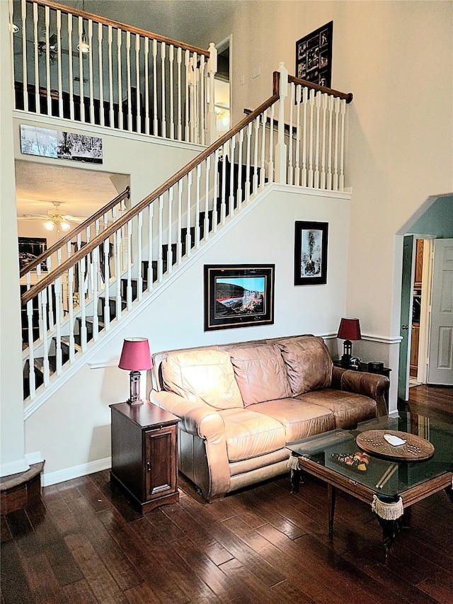 living room with stairs, a ceiling fan, hardwood / wood-style flooring, and a towering ceiling