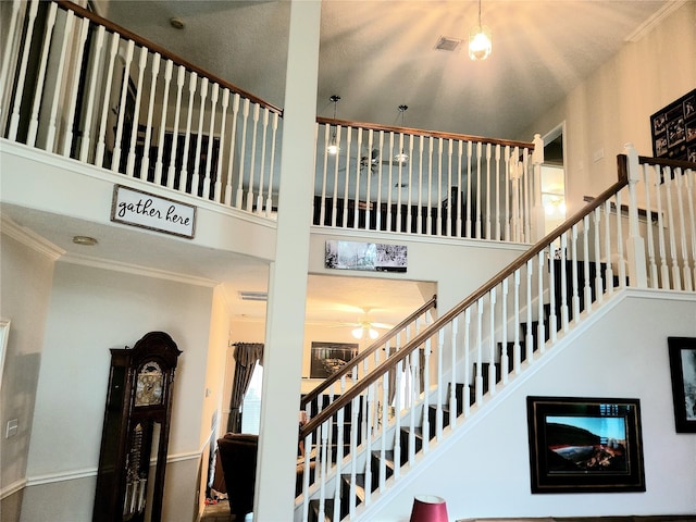 stairs with a high ceiling, ornamental molding, a ceiling fan, and visible vents