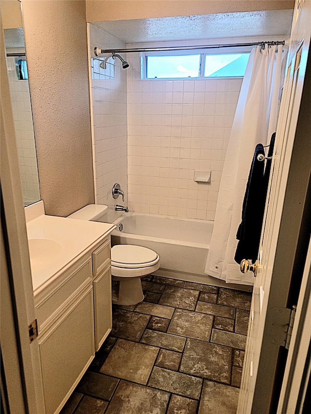 full bathroom featuring vanity, a textured wall, toilet, brick floor, and shower / bath combo