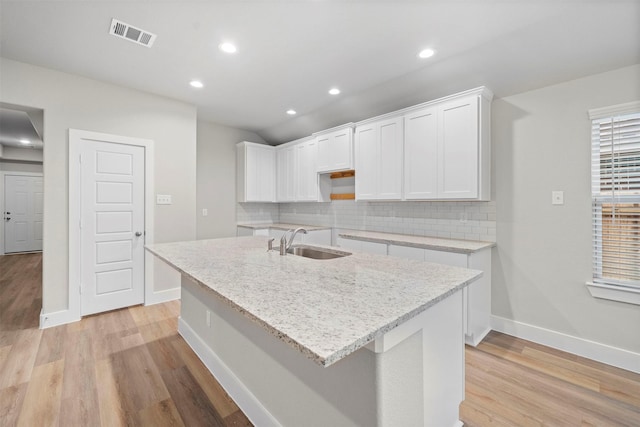 kitchen featuring backsplash, sink, a center island with sink, light hardwood / wood-style flooring, and white cabinetry