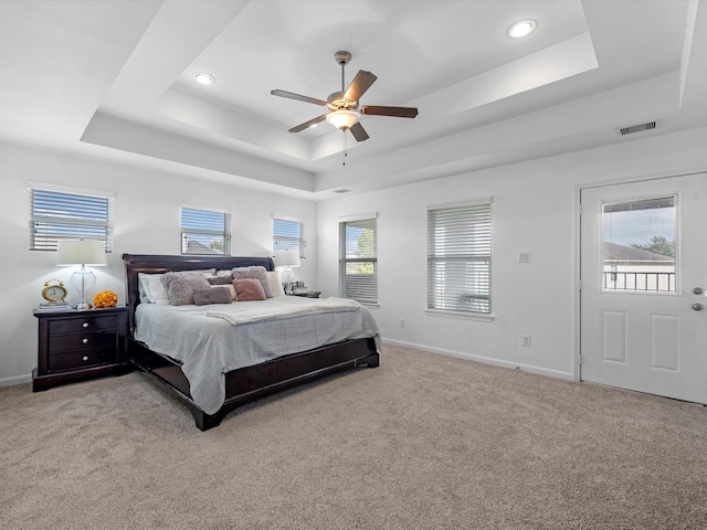 carpeted bedroom featuring ceiling fan, a raised ceiling, and multiple windows