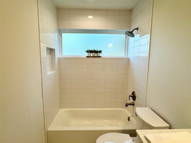 bathroom with toilet, tiled shower / bath, and a healthy amount of sunlight