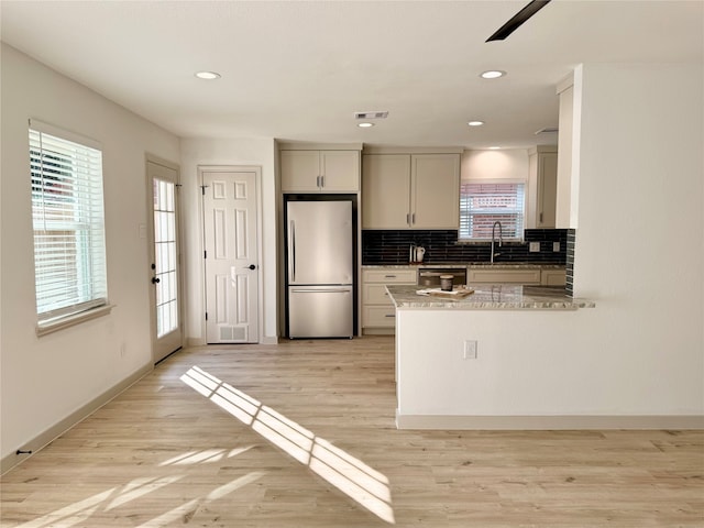 kitchen with stainless steel appliances, light hardwood / wood-style floors, light stone countertops, and decorative backsplash