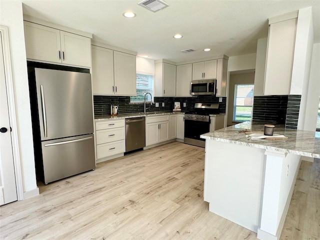 kitchen featuring kitchen peninsula, appliances with stainless steel finishes, light stone countertops, backsplash, and light wood-type flooring