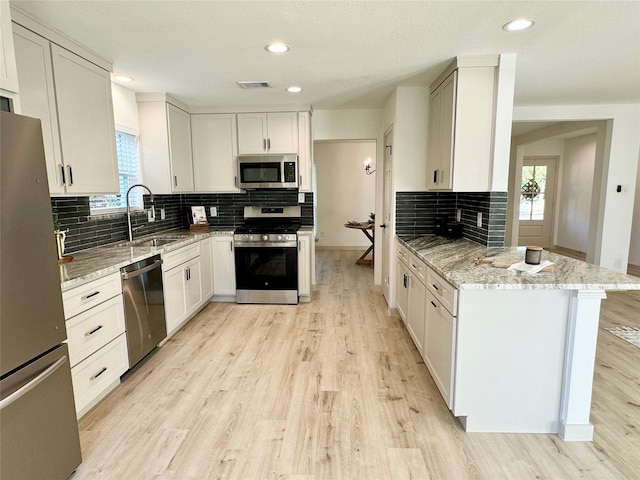 kitchen with stainless steel appliances, white cabinetry, light stone countertops, sink, and light hardwood / wood-style floors