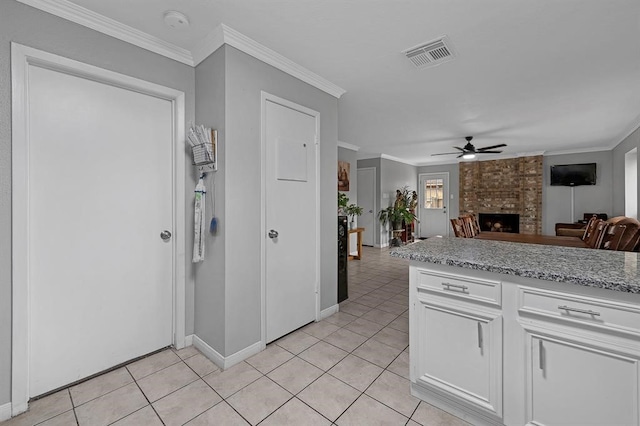 kitchen featuring light tile patterned floors, ceiling fan, ornamental molding, a brick fireplace, and white cabinetry