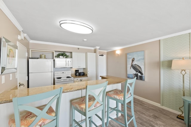 kitchen featuring white cabinets, a breakfast bar area, ornamental molding, light hardwood / wood-style floors, and white appliances