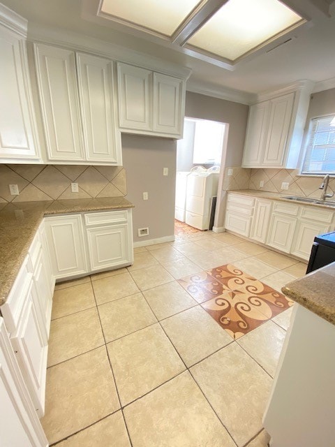 kitchen featuring crown molding, white cabinetry, washer and clothes dryer, and a healthy amount of sunlight