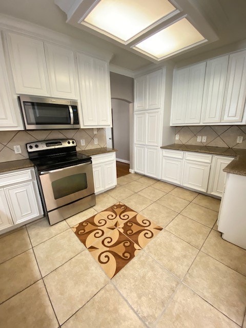 kitchen featuring light tile patterned floors, appliances with stainless steel finishes, white cabinets, and tasteful backsplash