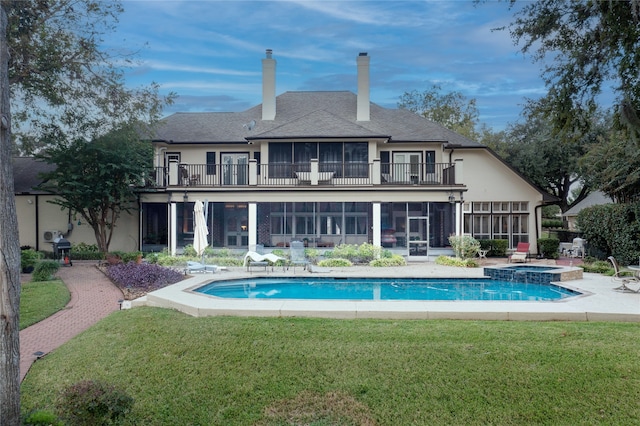 rear view of house with a pool with hot tub, a lawn, and a balcony