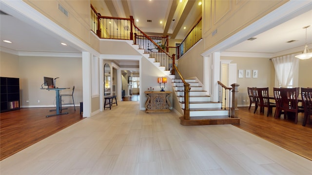 foyer entrance with ornamental molding, a high ceiling, and light wood-type flooring