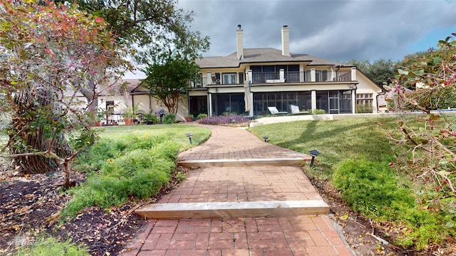 rear view of property featuring a balcony, a yard, and a sunroom