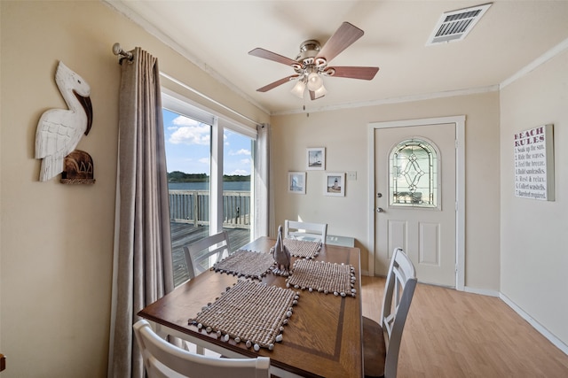 dining area featuring light hardwood / wood-style flooring, ceiling fan, a water view, and crown molding