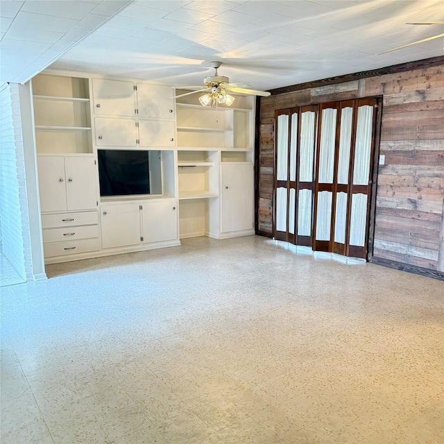 unfurnished living room featuring wooden walls, a ceiling fan, and light floors