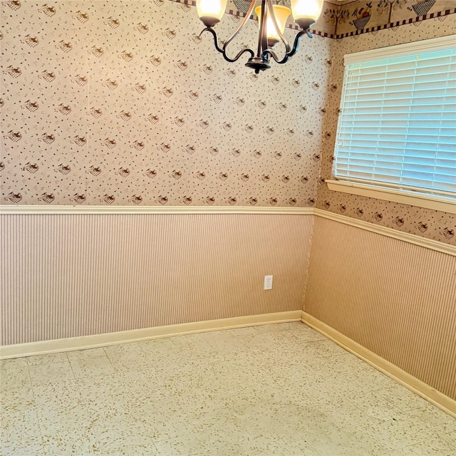 empty room with an inviting chandelier, wainscoting, and wallpapered walls
