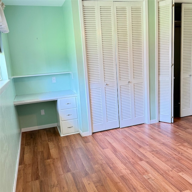 unfurnished bedroom featuring light wood finished floors, built in desk, and baseboards