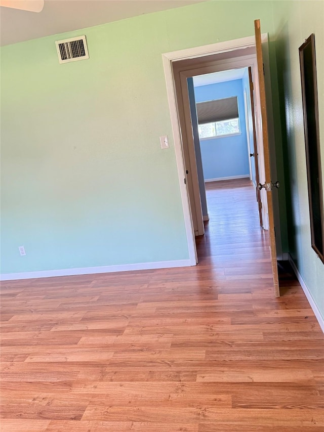 hall with light wood-style floors, visible vents, and baseboards