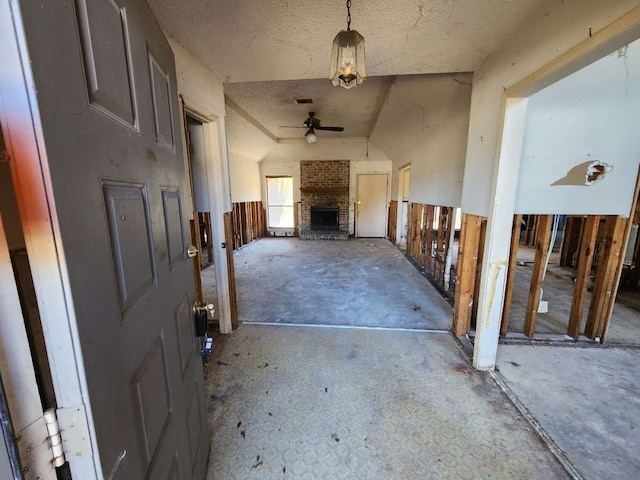 interior space featuring ceiling fan, a textured ceiling, lofted ceiling, and a brick fireplace