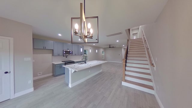 kitchen with sink, light stone counters, ceiling fan with notable chandelier, and light wood-type flooring