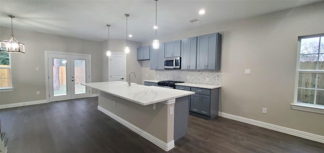 kitchen with pendant lighting, range, french doors, tasteful backsplash, and a center island with sink