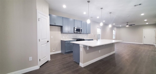 kitchen featuring dark hardwood / wood-style flooring, decorative light fixtures, tasteful backsplash, a kitchen island with sink, and a breakfast bar