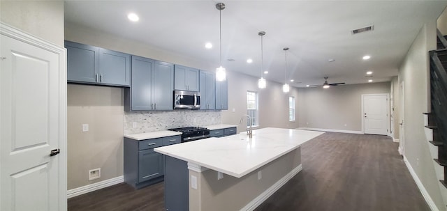 kitchen with decorative light fixtures, decorative backsplash, dark hardwood / wood-style floors, light stone counters, and a center island with sink