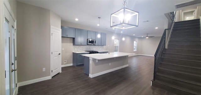 kitchen featuring a kitchen island with sink, stove, pendant lighting, backsplash, and dark hardwood / wood-style floors