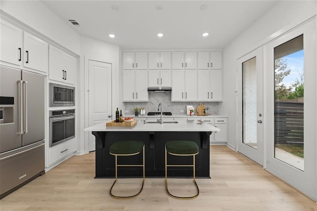 kitchen featuring french doors, appliances with stainless steel finishes, a kitchen island with sink, decorative backsplash, and white cabinets