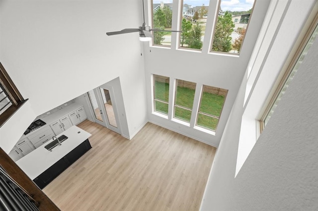 unfurnished living room featuring sink, light hardwood / wood-style floors, a high ceiling, and a wealth of natural light