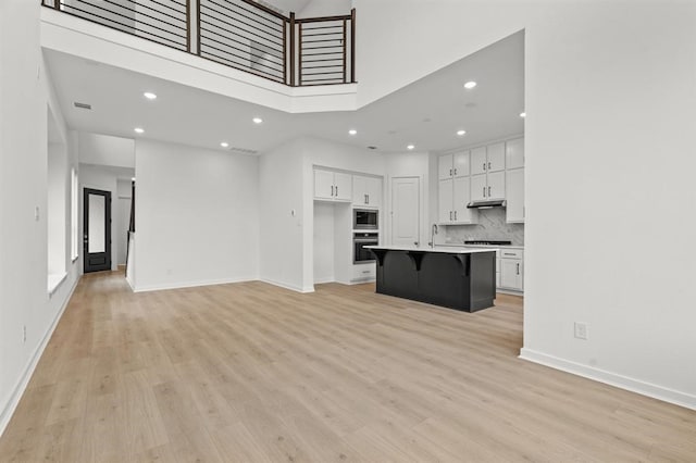 unfurnished living room featuring a high ceiling, sink, and light wood-type flooring