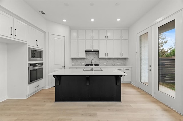 kitchen with built in microwave, white cabinetry, a kitchen island with sink, and oven