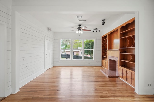 unfurnished living room with light hardwood / wood-style floors, ceiling fan, and wooden walls