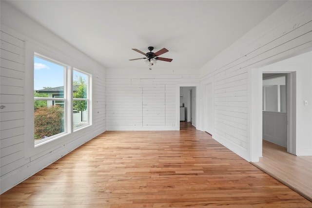 spare room featuring light wood-type flooring, wood walls, and ceiling fan