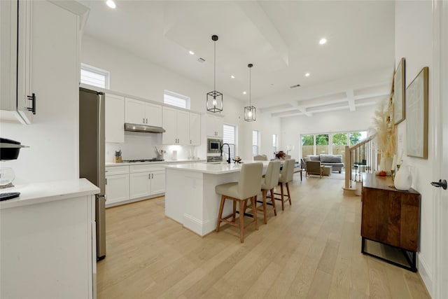 kitchen featuring white cabinetry, light wood-type flooring, beam ceiling, pendant lighting, and an island with sink