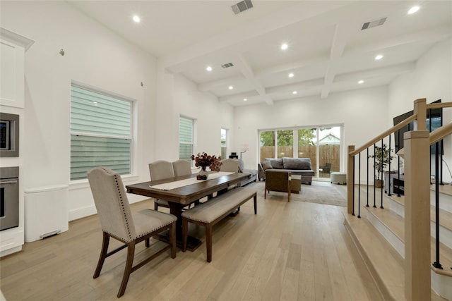 dining space featuring a towering ceiling, beamed ceiling, light wood-type flooring, and coffered ceiling