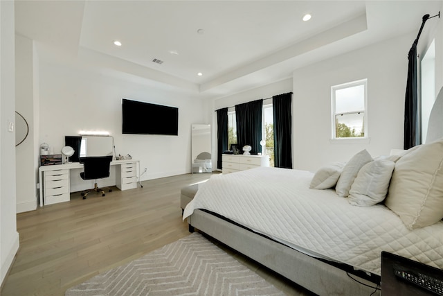 bedroom with light wood-type flooring and a raised ceiling