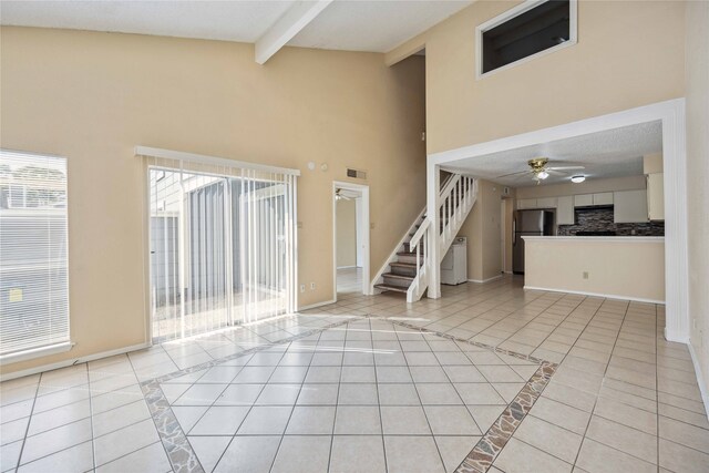 unfurnished living room featuring beamed ceiling, light tile patterned floors, a textured ceiling, high vaulted ceiling, and ceiling fan