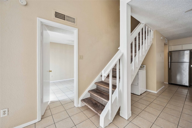 stairway with washer / clothes dryer, a textured ceiling, and tile patterned floors