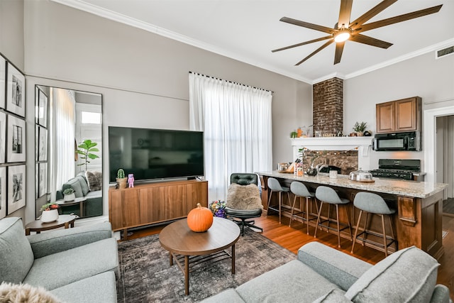 living room featuring crown molding, dark wood-type flooring, a fireplace, and ceiling fan