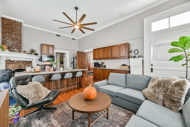 living room with dark wood-type flooring, ceiling fan, ornamental molding, and a fireplace
