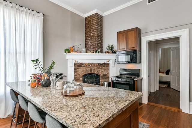 kitchen featuring dark hardwood / wood-style floors, ornamental molding, black appliances, light stone countertops, and a fireplace