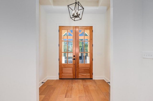 entryway with french doors, a chandelier, a tray ceiling, and light wood-type flooring