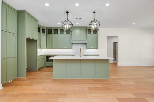 kitchen with a center island with sink, light hardwood / wood-style flooring, custom range hood, decorative light fixtures, and green cabinetry