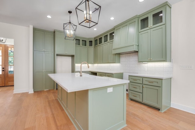 kitchen with decorative backsplash, an island with sink, light hardwood / wood-style flooring, green cabinets, and pendant lighting